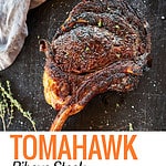 Seared Tomahawk Steak on black platter with herbs.