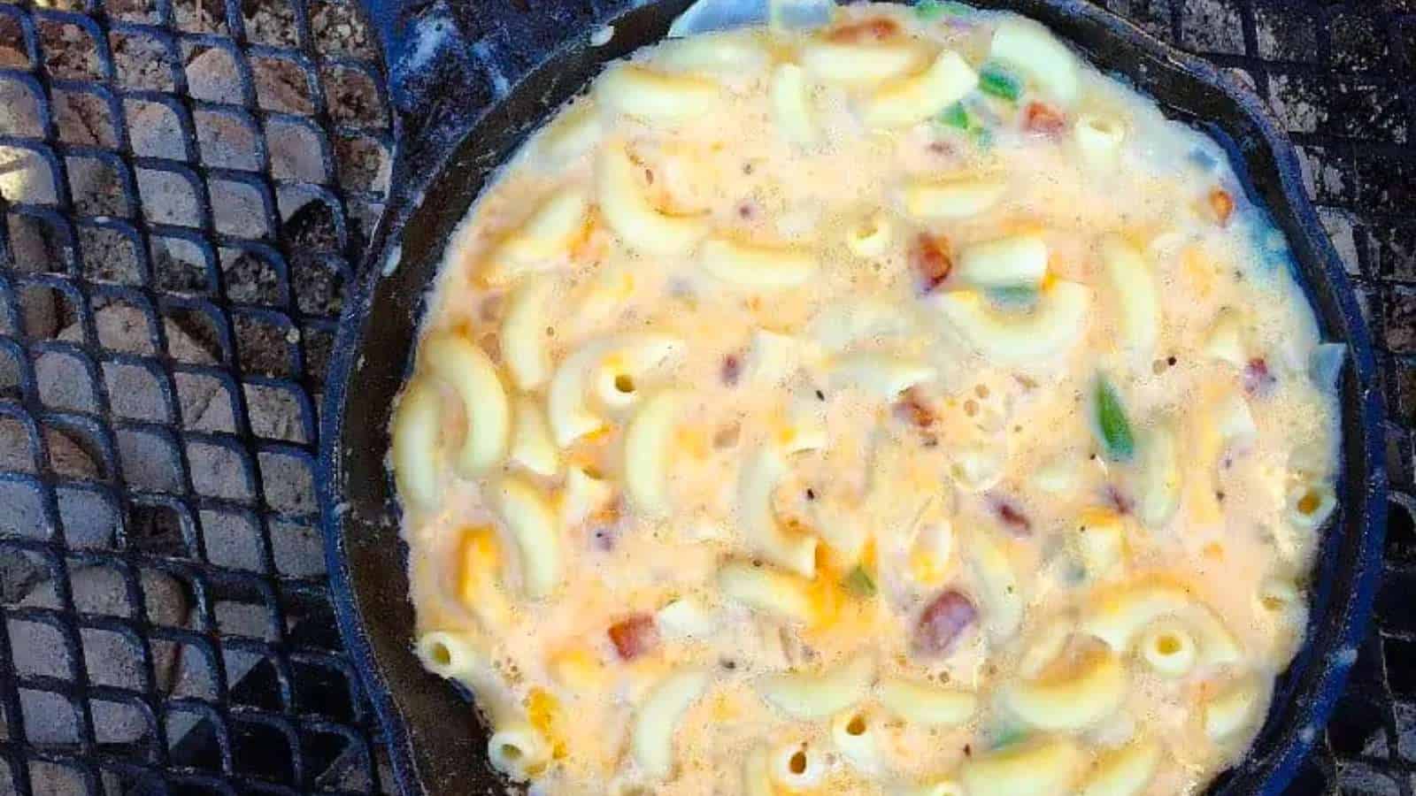 cast iron skillet of mac and cheese over a campfire.