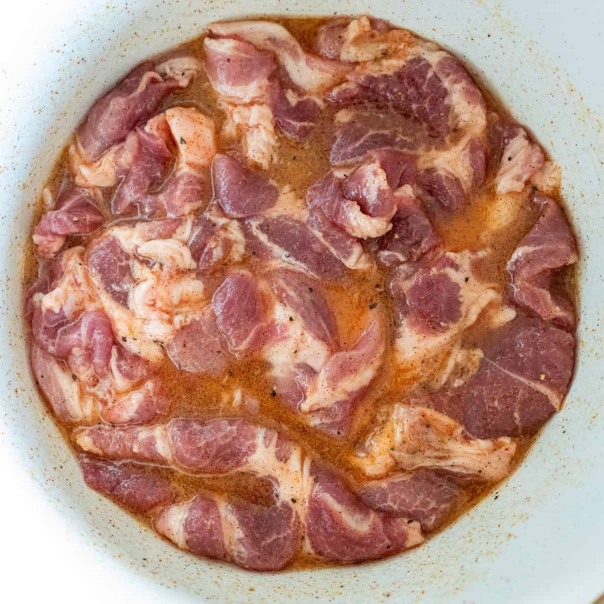 Pork steaks marinating in bowl of tocino marinade.