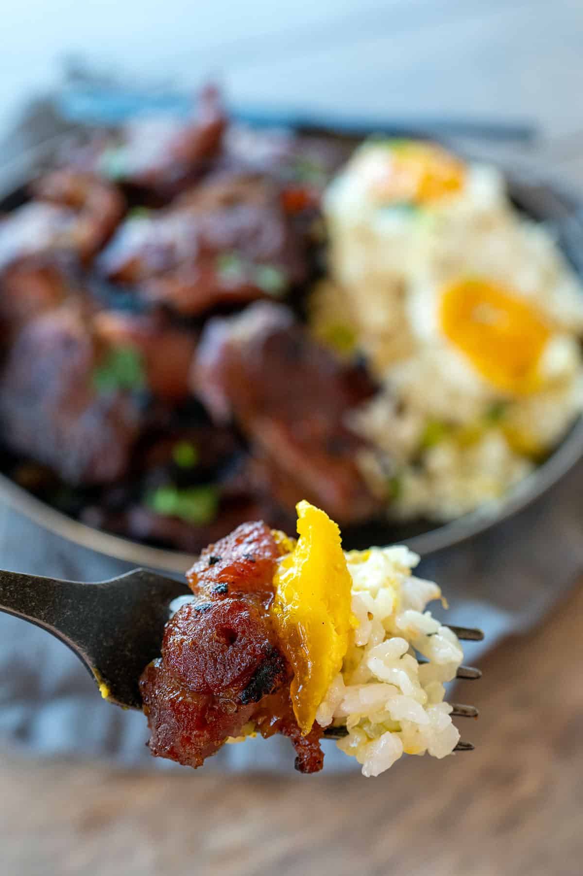 Fork full of pork tocino with garlic fried rice and fried eggs.