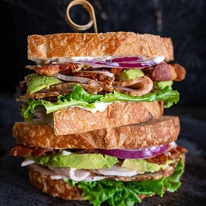 Two turkey sandwiches with bacon and avocado stacked on top of each other.