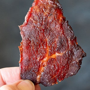 Hand holding piece of smoked Big Red chipotle beef jerky.