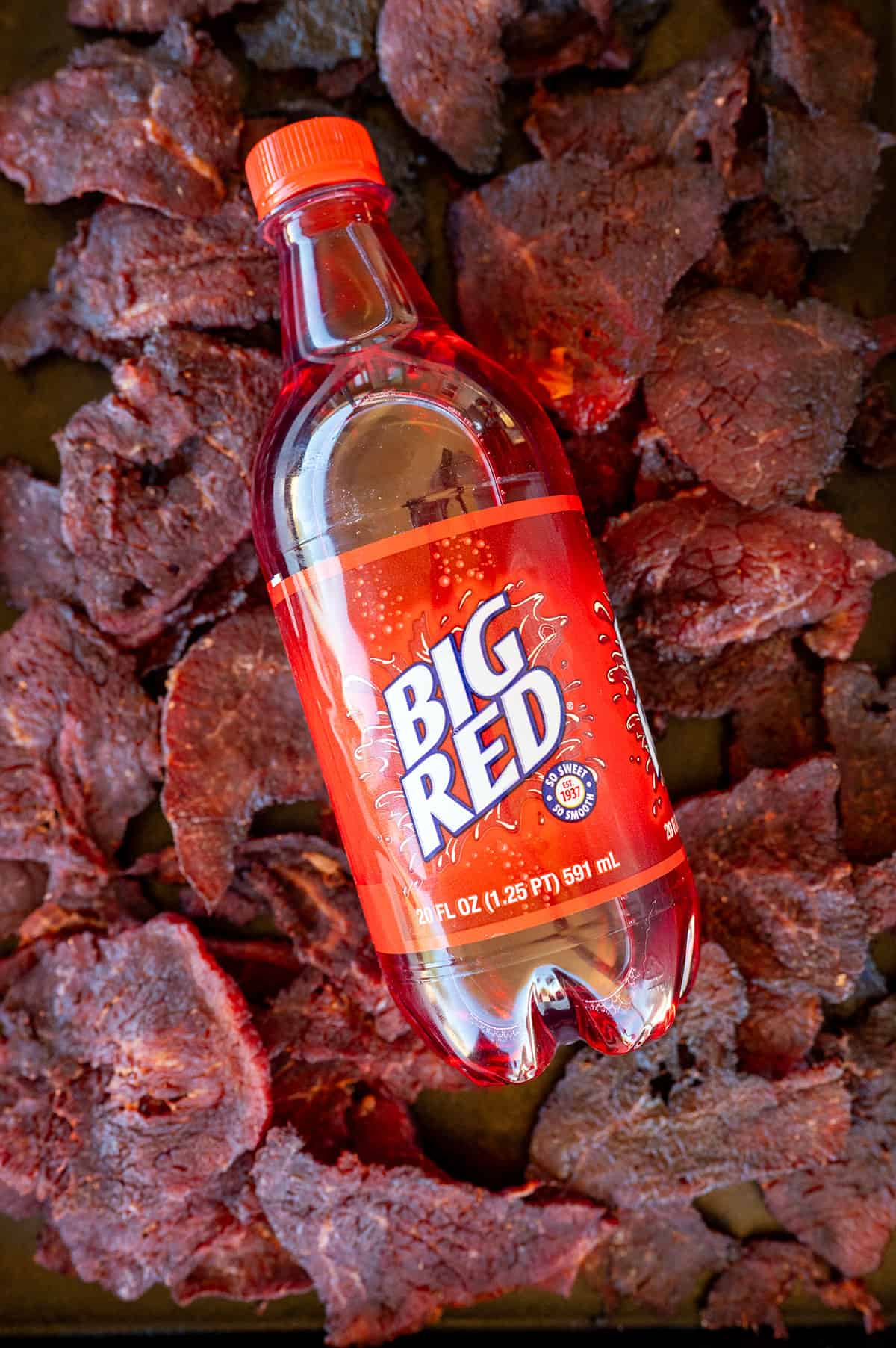 Tray of Big Red beef jerky with bottle of soda laying on top.