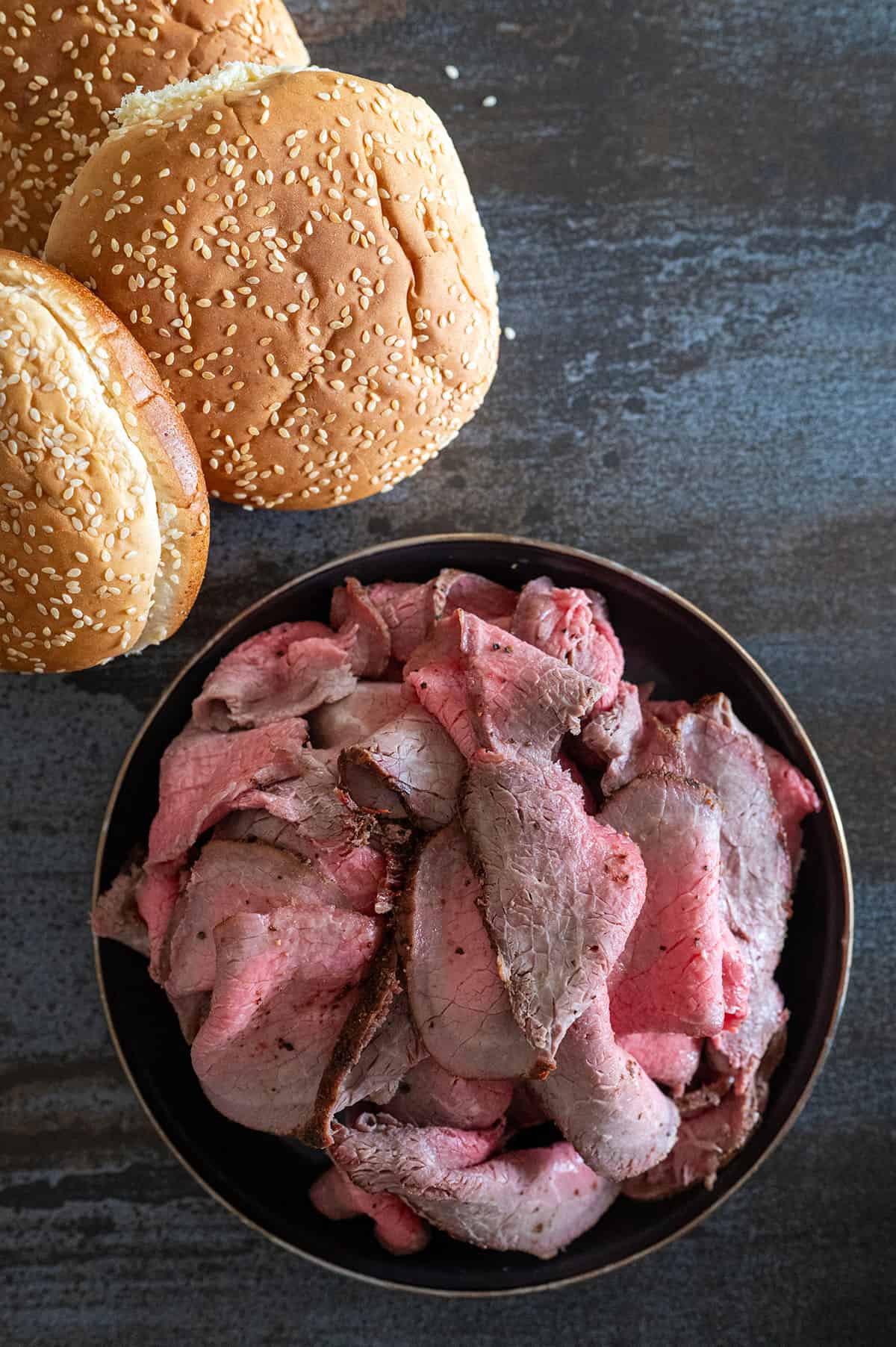 Plate of sliced roast beef next to sesame seed buns.