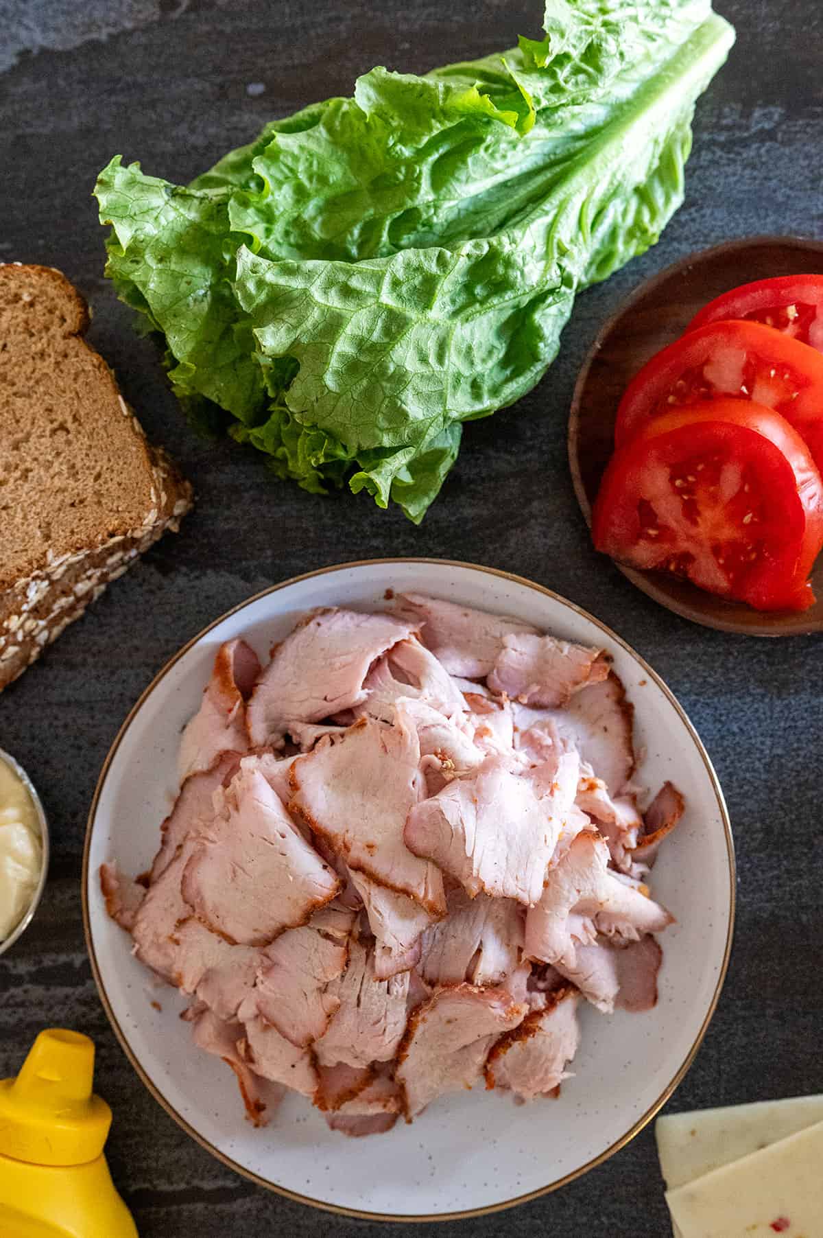 Plate of smoked pork lunch meat surrounded by sandwich ingredients.