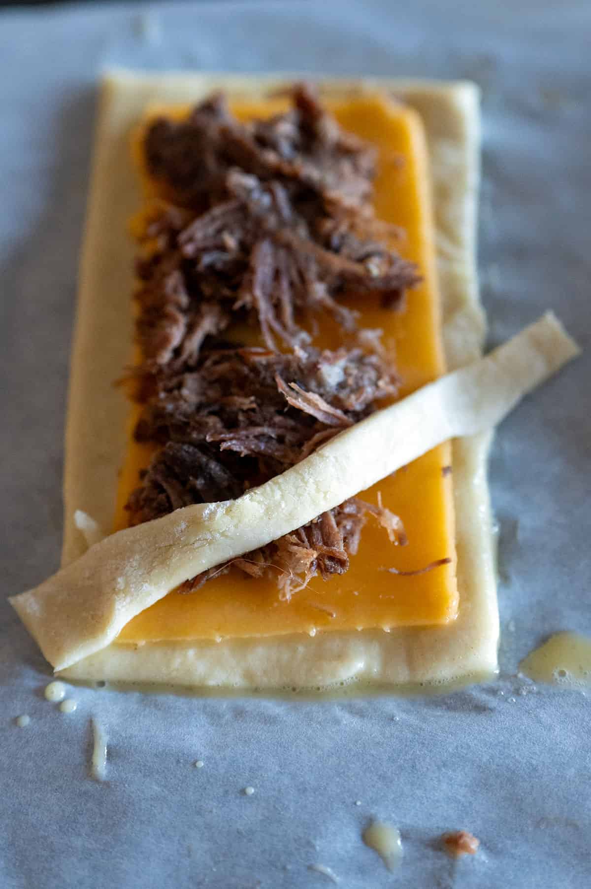 One thin strip of puff pastry laid over brisket and cheese.
