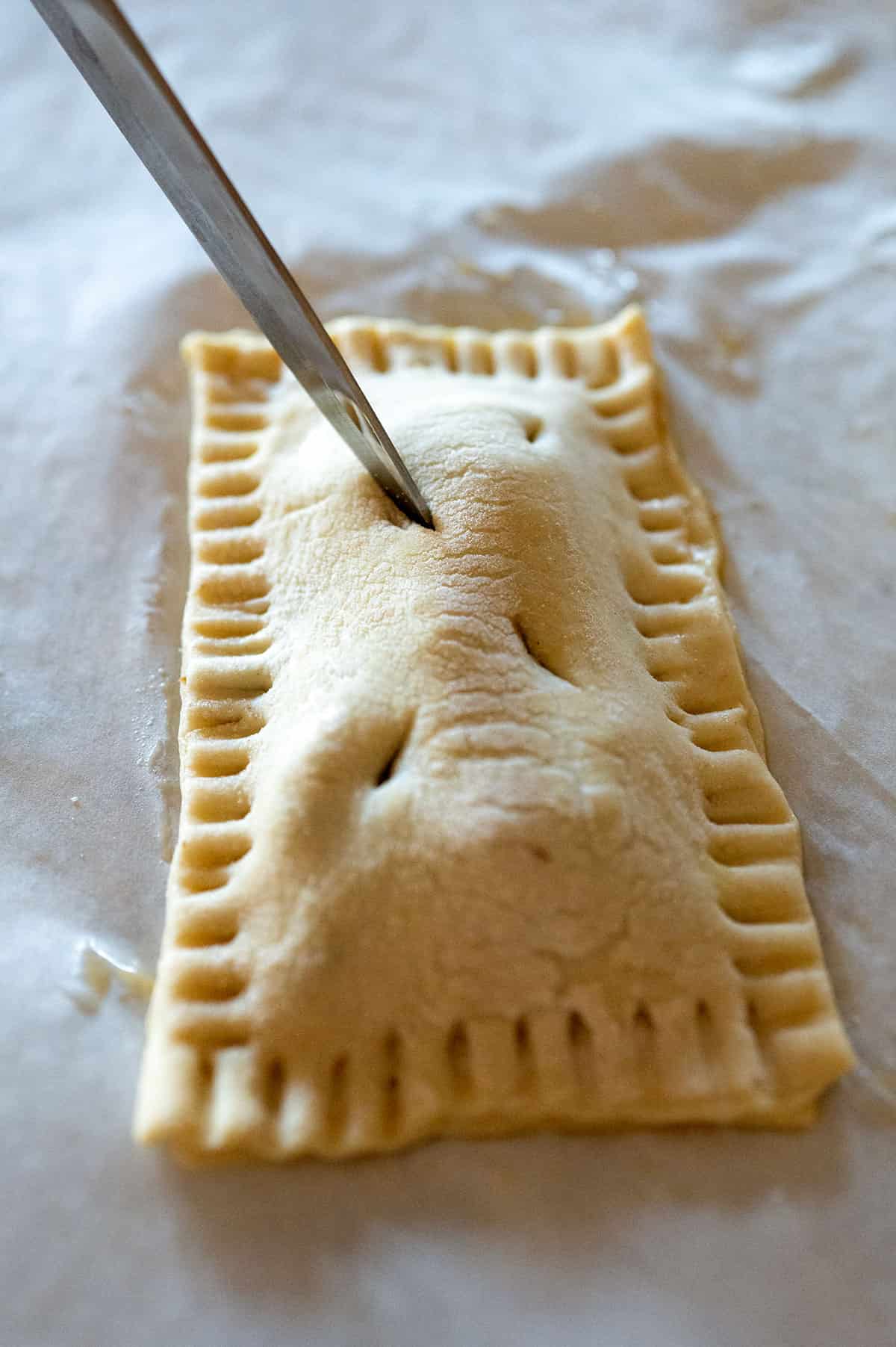 Piercing top layer of puff pastry with a knife.