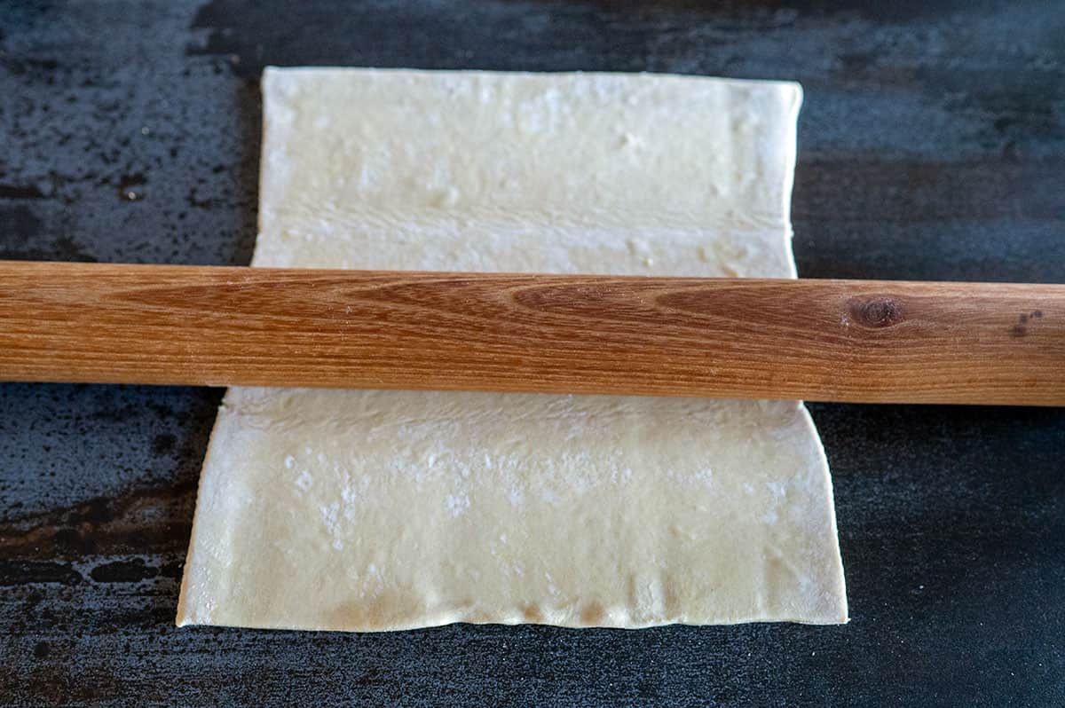 Rolling puff pastry flat with rolling pin.