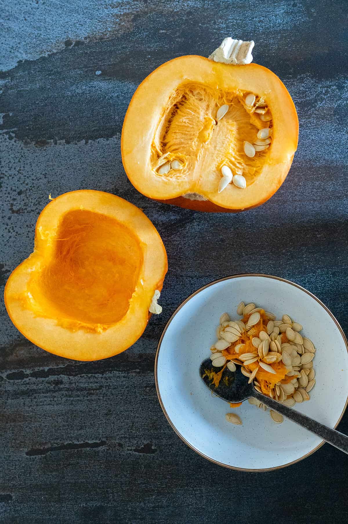 Using spoon to scoop pumpkin seeds out of pumpkin half.