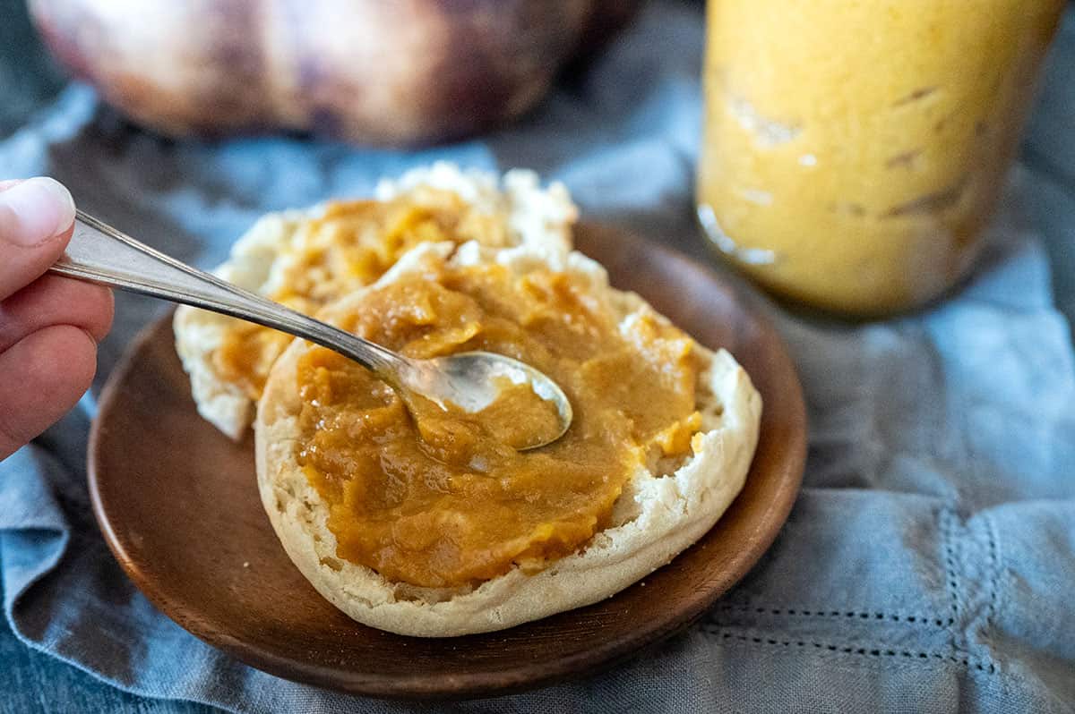 Using a spoon to spread pumpkin butter on an English muffin.