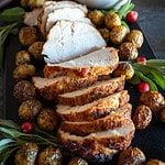 Sliced turkey breast roast on platter with roasted potatoes and gravy.