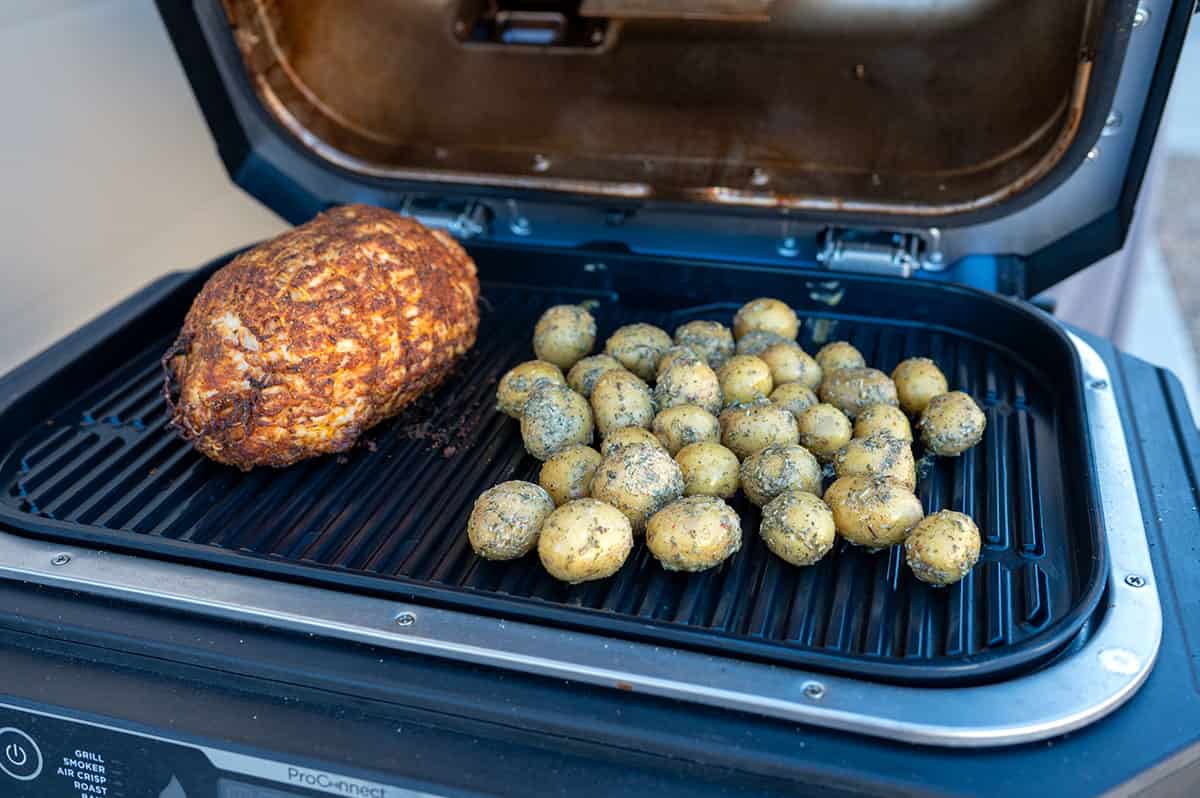Seasoned potatoes next to turkey breast roast on Ninja Grill.