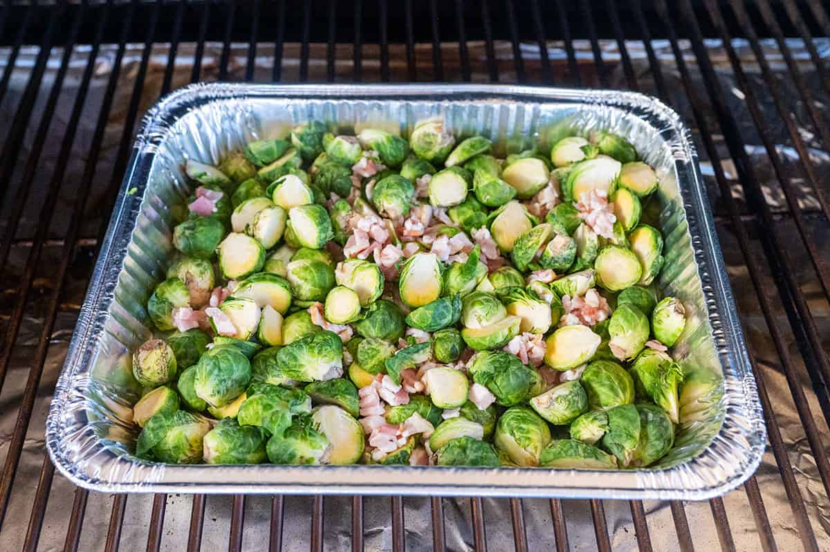 raw brussel sprouts halves in pan on grill with bacon.