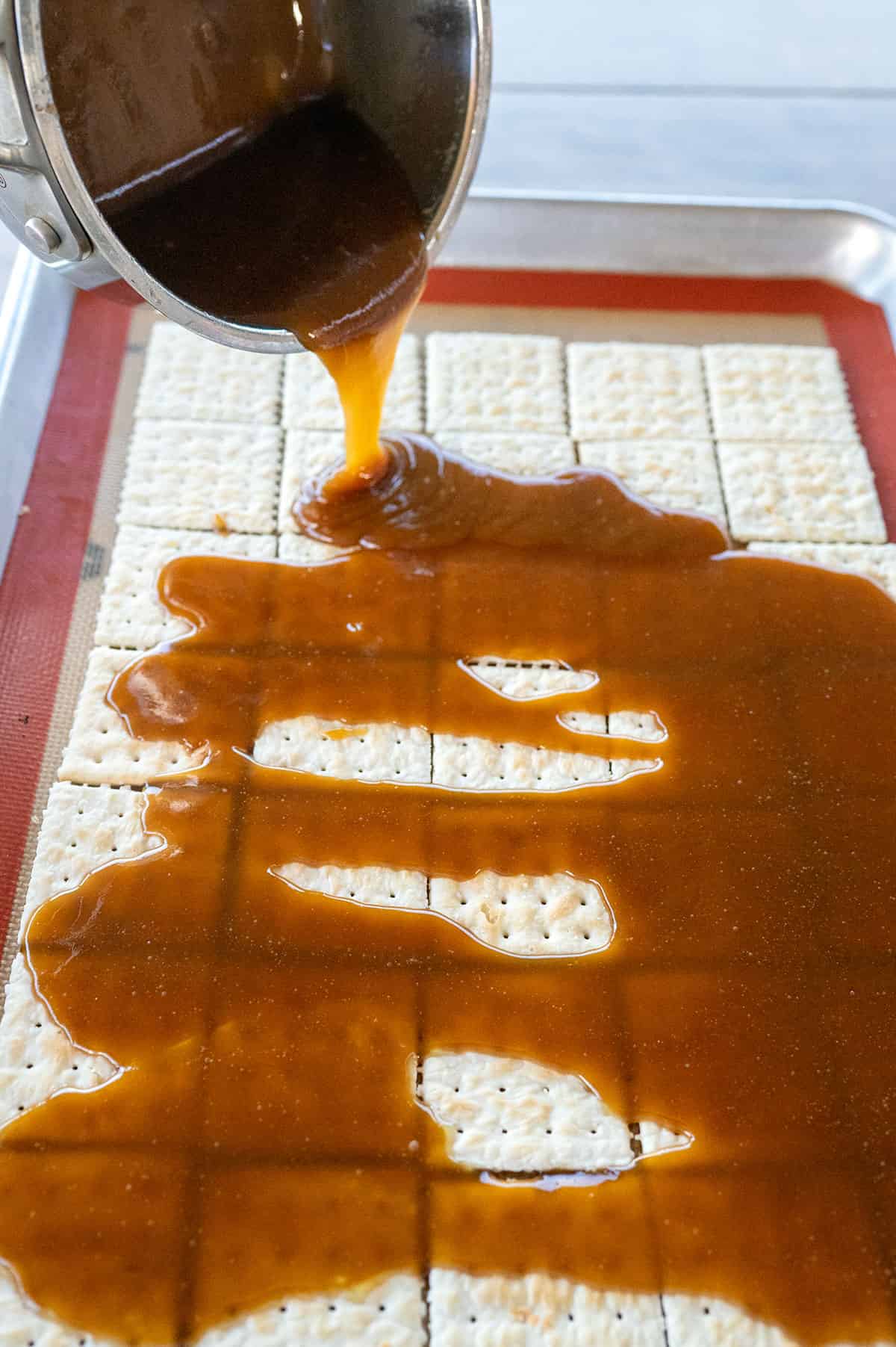 Pouring pan of toffee on crackers on pan.