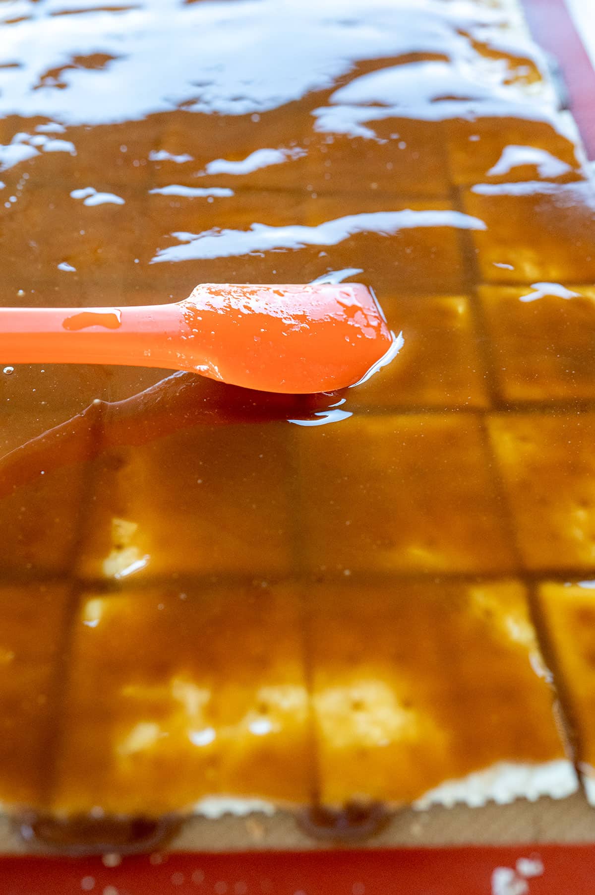 Using a spatula to spread toffee on crackers.