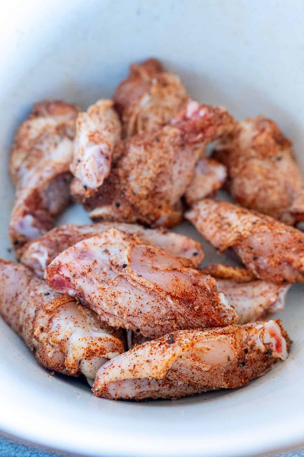 Raw chicken wings rubbed with chicken wing dry rub in white bowl.
