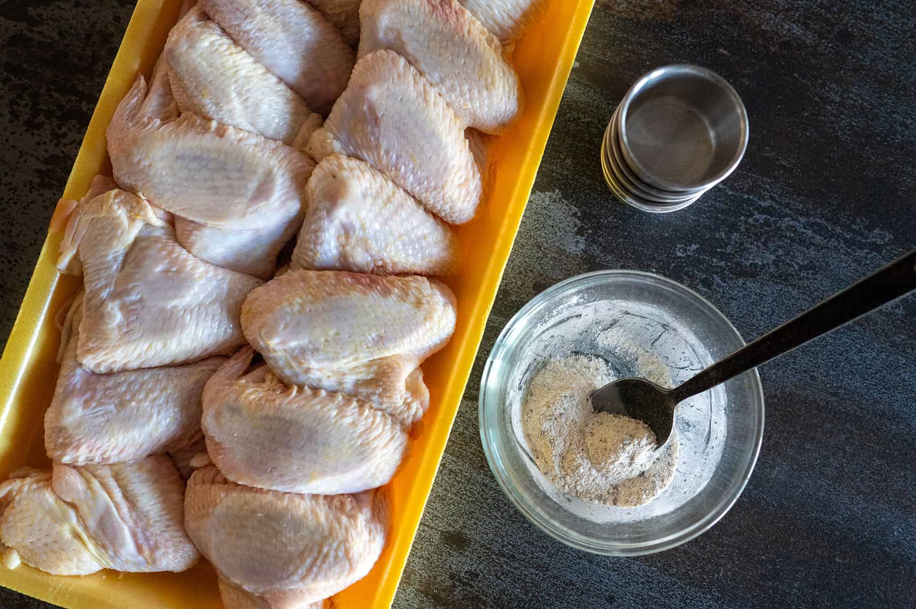 Crispy chicken wing rub in bowl next to wings.