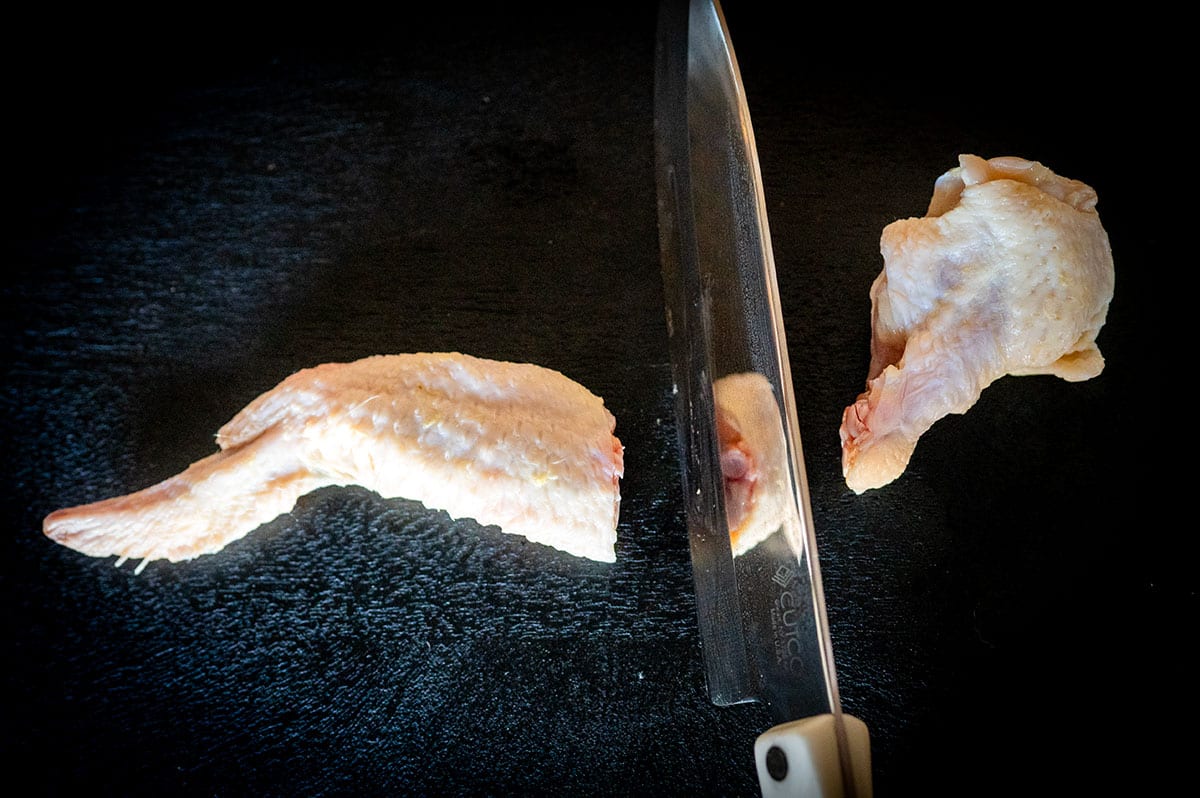 Using a chef's knife to separate a chicken wing flat from a wing drum.