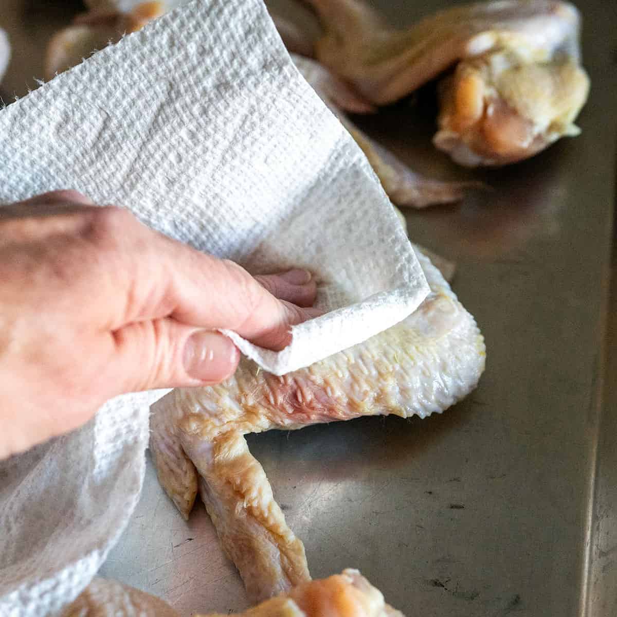 patting a chicken wing dry with a paper towel.