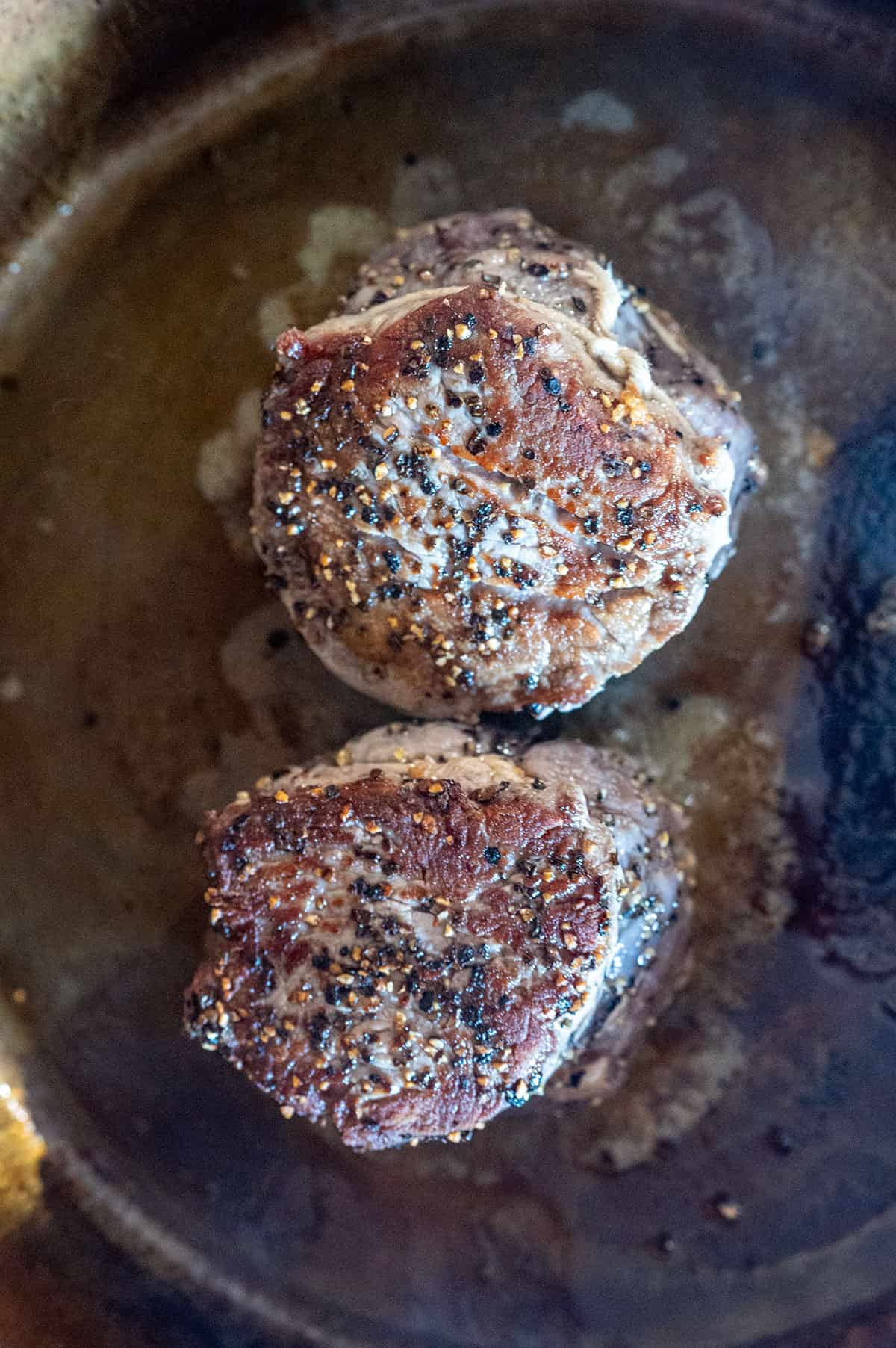 2 filet mignon steaks searing in cast iron skillet.