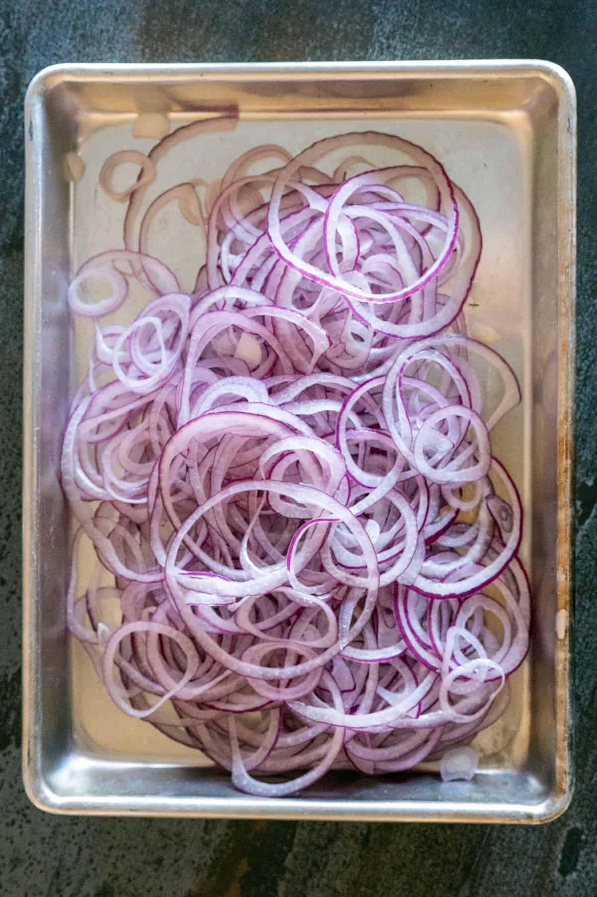 Sheet pan of thinly sliced red onions.