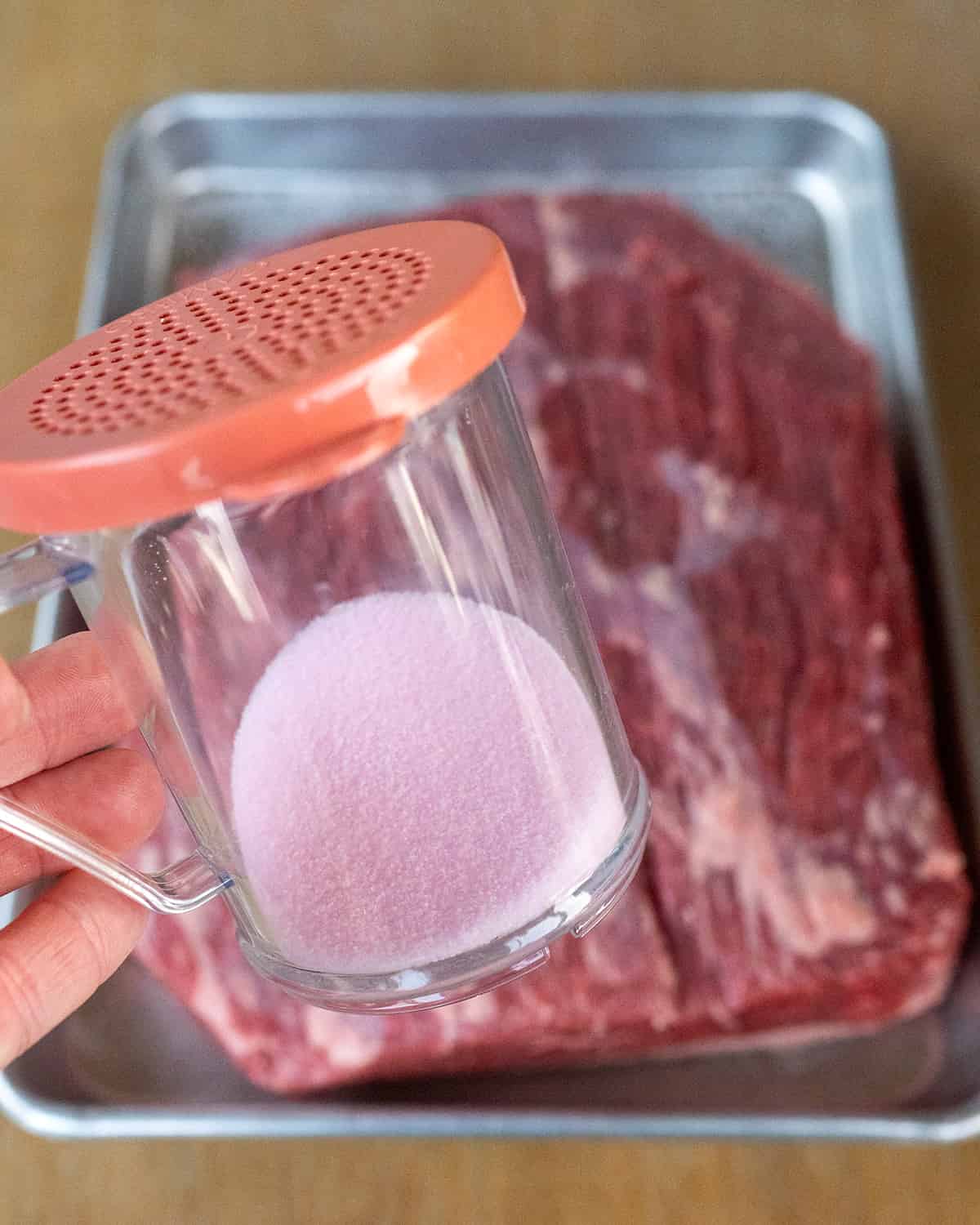 Shaker of pink curing salt over brisket.