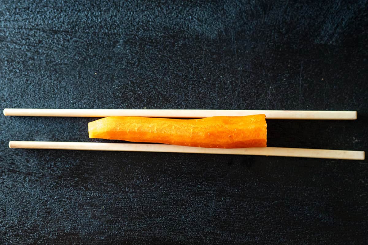 Carrot on cutting board between two chopsticks.