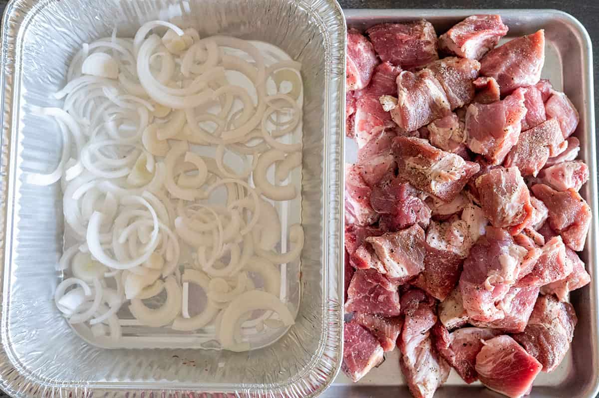 Seasoned pork butt on pan next to sliced onions in pan. 