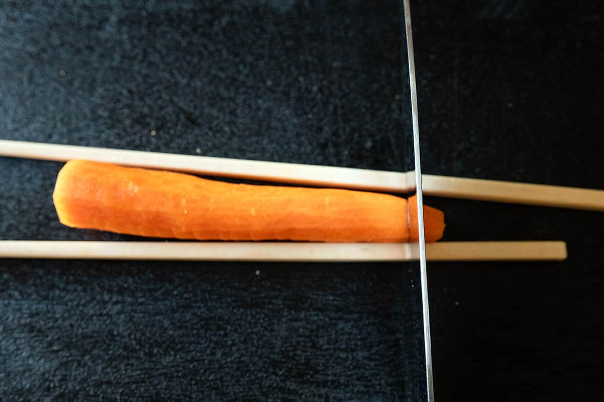 Carrot on cutting board between two chopsticks. Slicing at 90-degree angle.