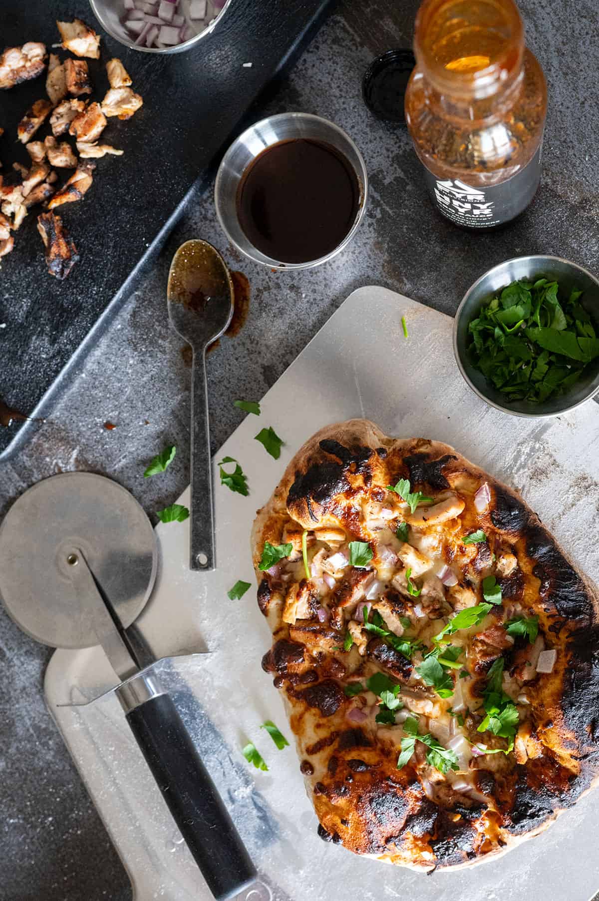 Whole bbq chicken pizza on platter with ingredients.