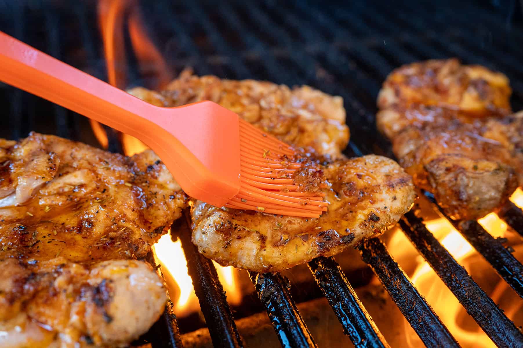 Basting chicken thighs on grill.