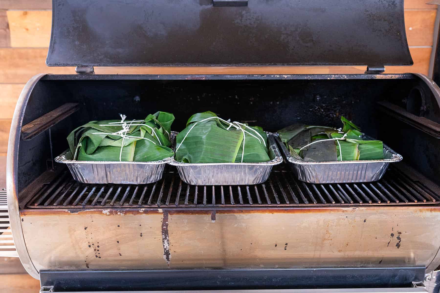 three pans of kalua pork on pellet grill.