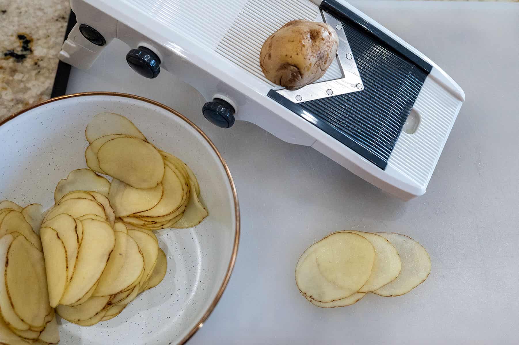 Using mandoline to slice potatoes very thin.