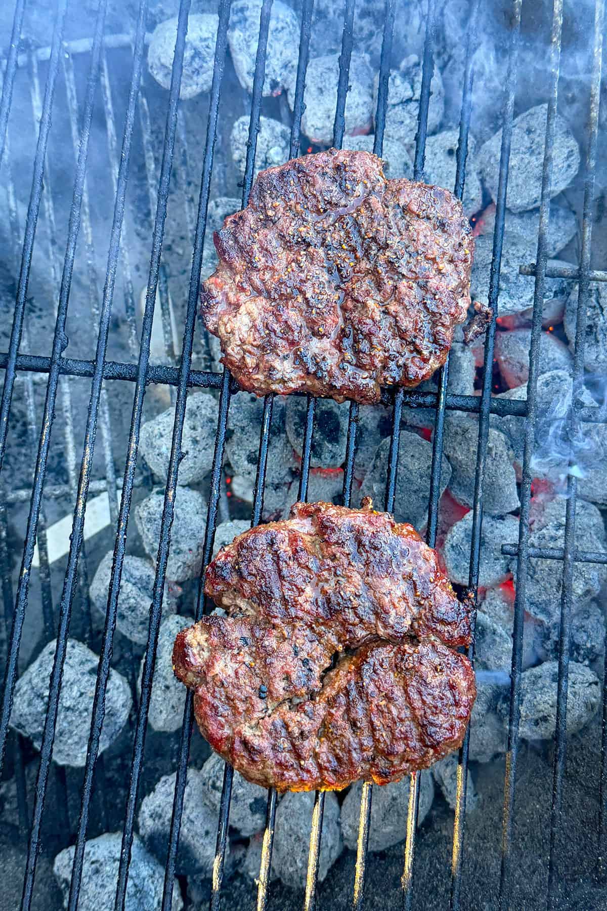 2 burgers cooking on grill over charcoal.
