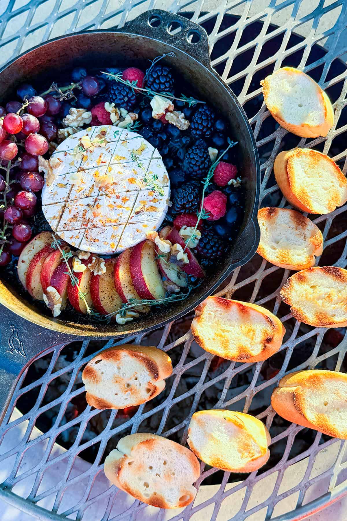 Bread slices toasting next to skillet of brie cheese and fruit.