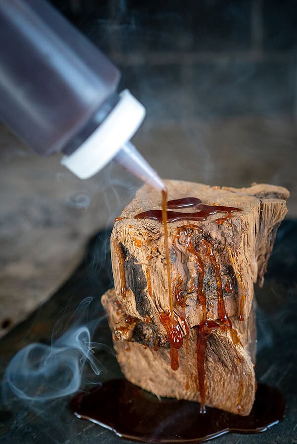 Drizzling hot honey on wood with smoke in background.