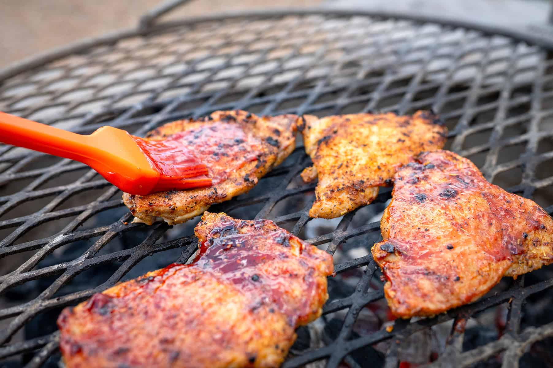 brushing raspberry chipotle sauce on chicken thighs on grill.