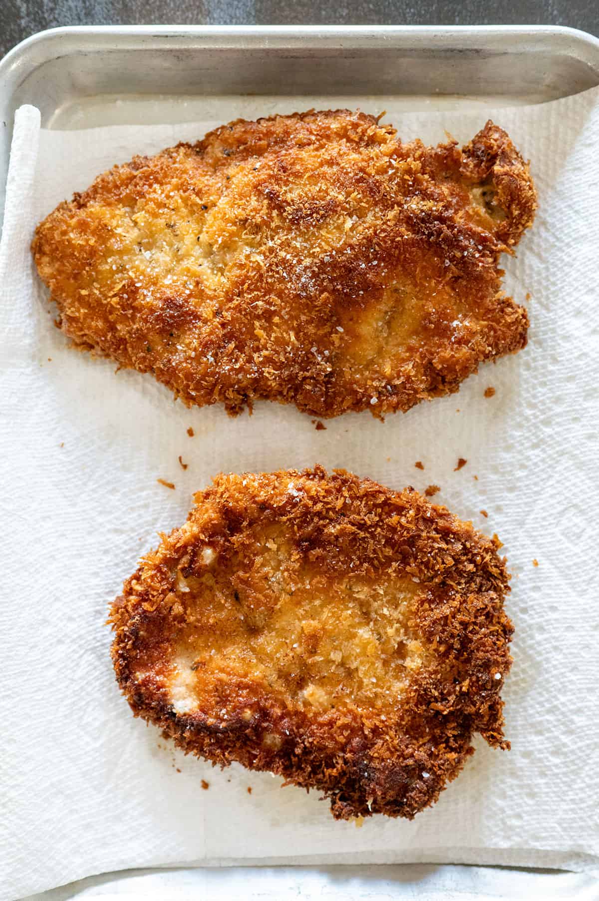 2 pieces of fried pork schnitzel on paper towel.