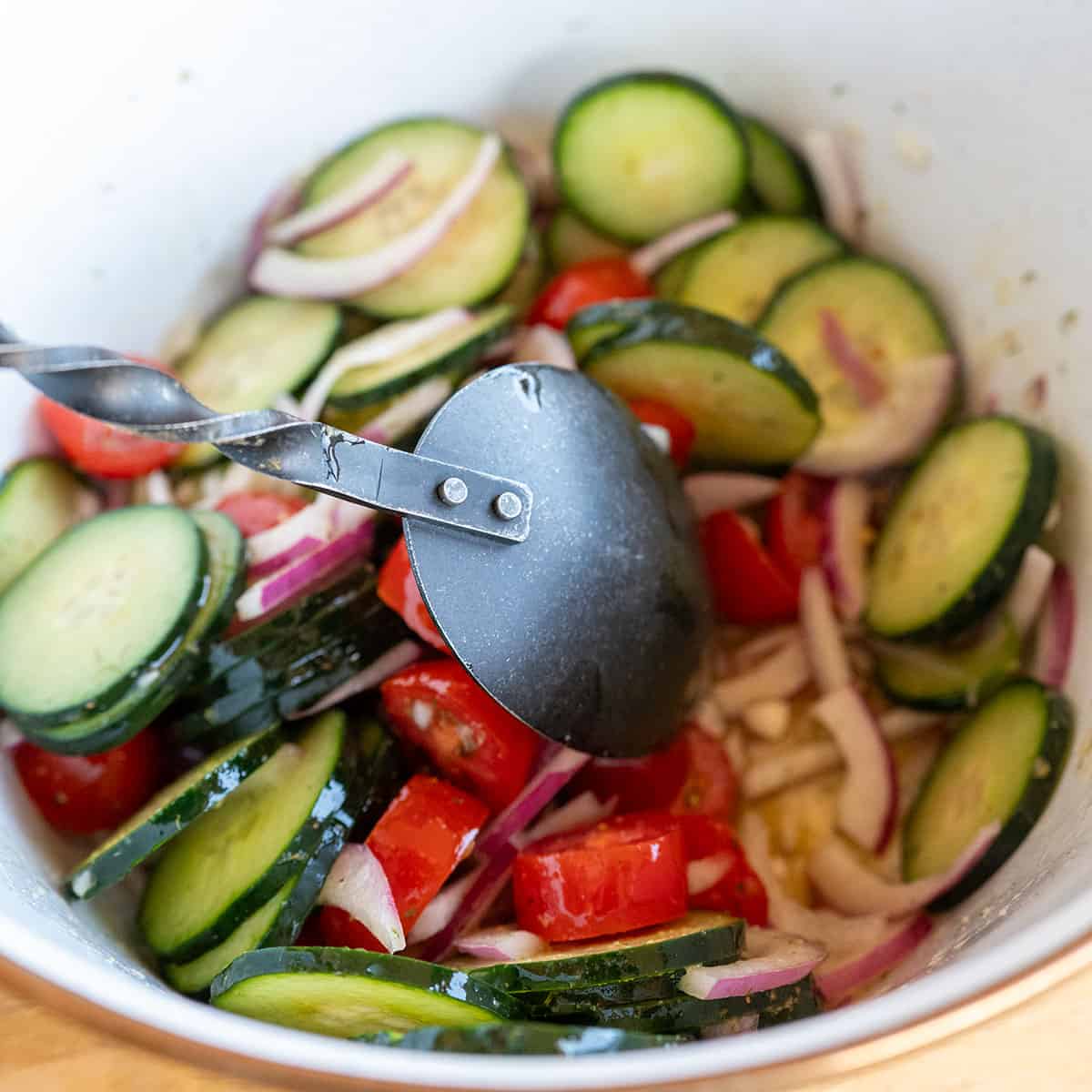 Tossing cucumbers, onions and tomatoes with dressing.